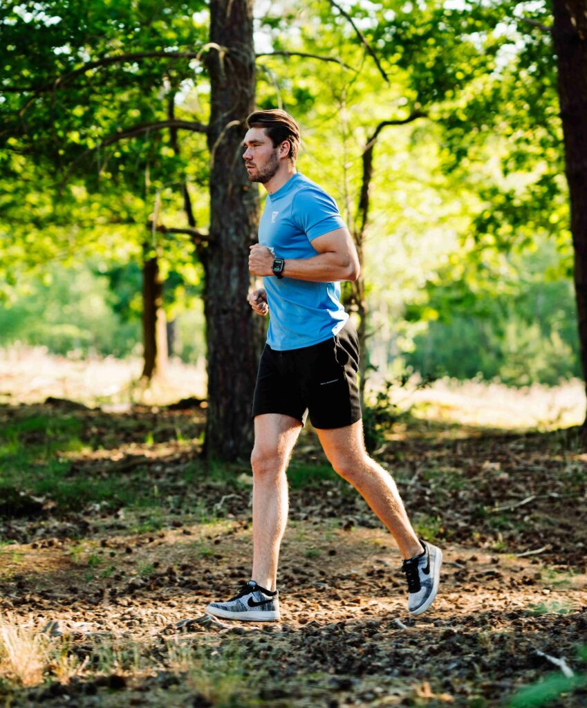 Läufer im blauen Shirt auf einem Waldweg – Joggen lernen im ruhigen Tempo