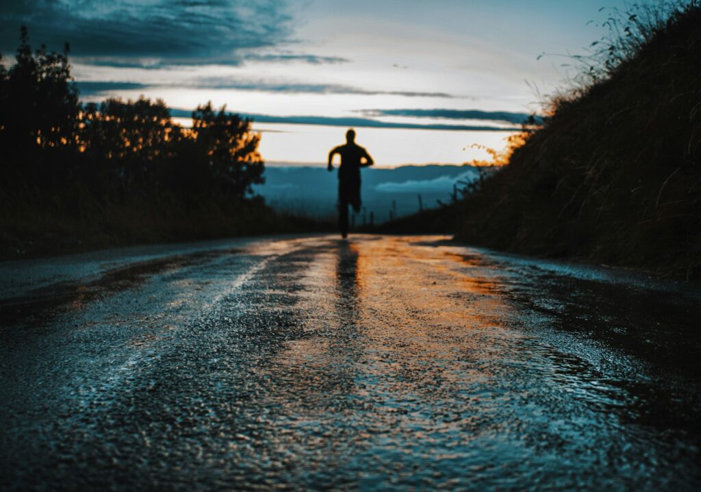 Silhouette einer joggenden Person auf einer Straße im Gegenlicht – Joggen-Vorteile für die Gesundheit