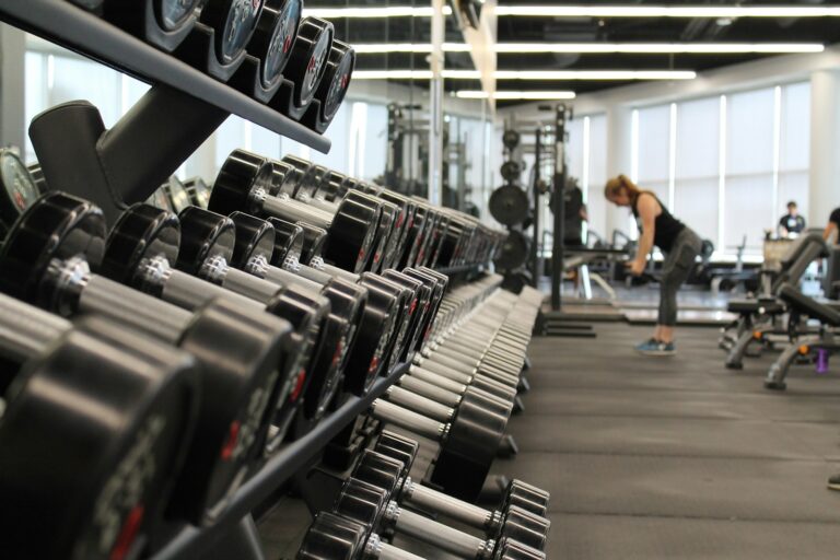 Frau im Fitnessstudio zwischen Hanteln und Geräten vor dem Krafttraining jeden Tag