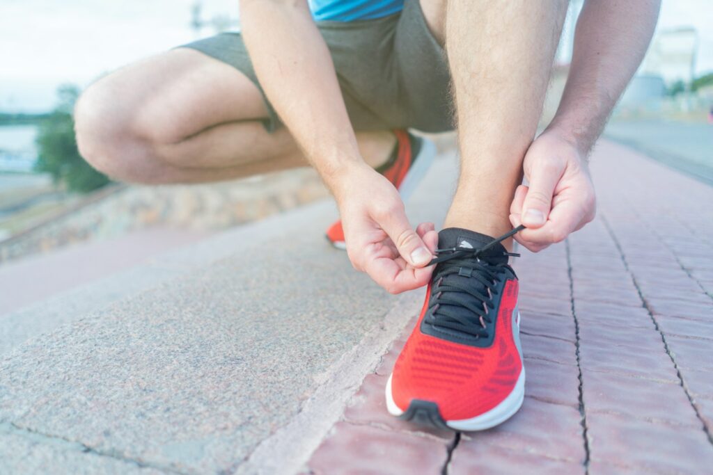 Person in roten Sneakern sitzt vor dem Training auf Betonboden – Motivation zum Sport beginnt mit dem ersten Schritt