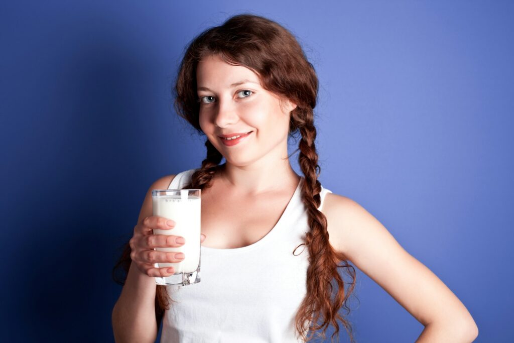 Protein Shake wann nehmen: junge Frau hält ein Glas mit einem milchigen Getränk