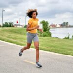 Frau joggt auf einer Straße am See – Sport und Psyche im Einklang