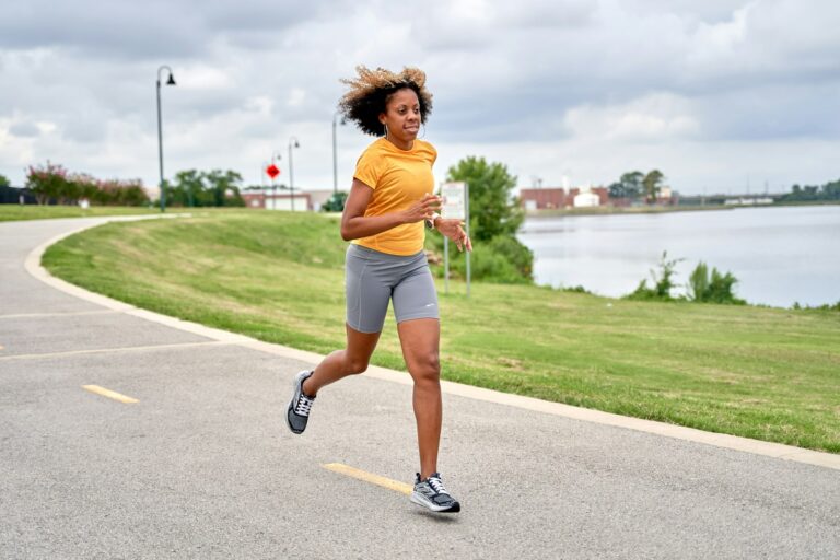Frau joggt auf einer Straße am See – Sport und Psyche im Einklang