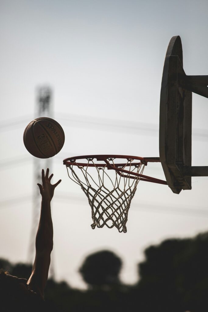 Basketball fliegt auf den Korb zu, eine Hand streckt sich danach aus