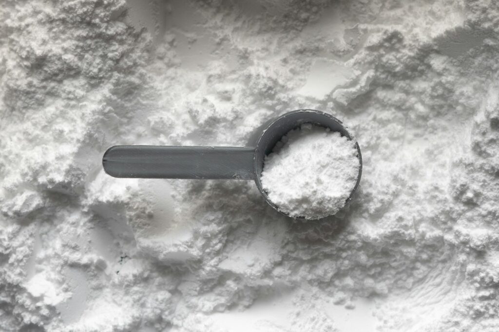 Messlöffel mit weißem Pulver wie Kreatin auf einem Pulverhaufen, welche Supplements brauche ich