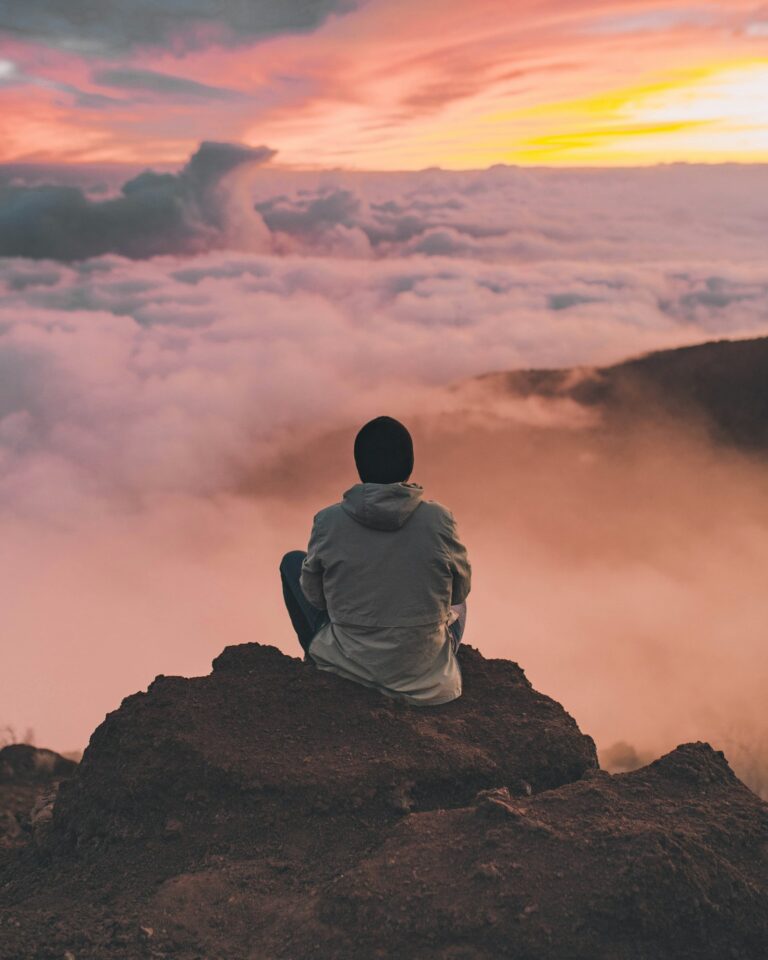 Person sitzt auf einem Felsen über den Wolken – Sinnbild für Trainingsziele setzen mit Weitblick